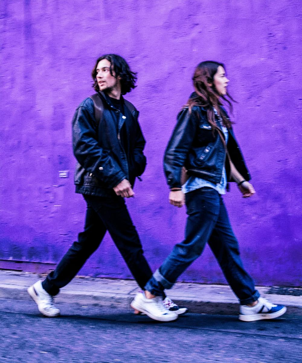 Two people walking past a purple wall with motion blur